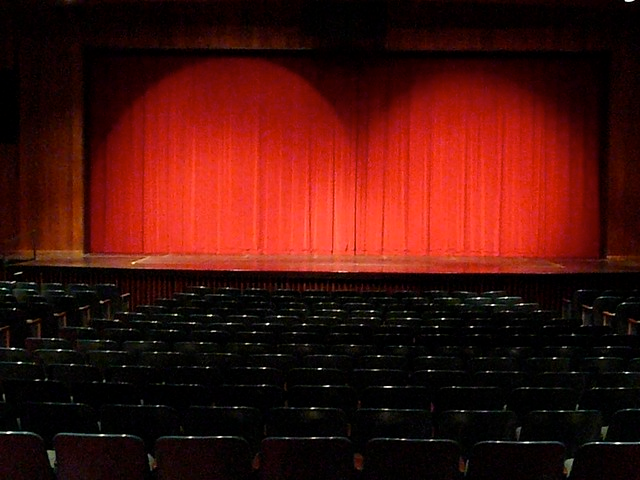 Image of an open theatre, facing the stage or screen, with red curtains closed